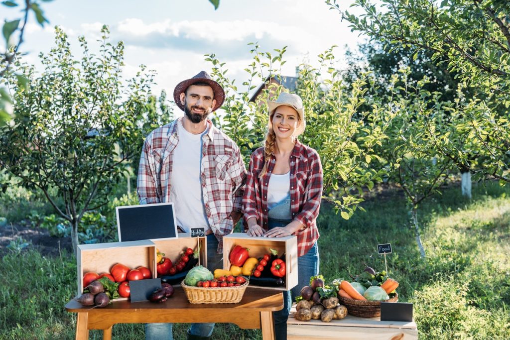 two smiling farmers selling locally grown vegetables at market