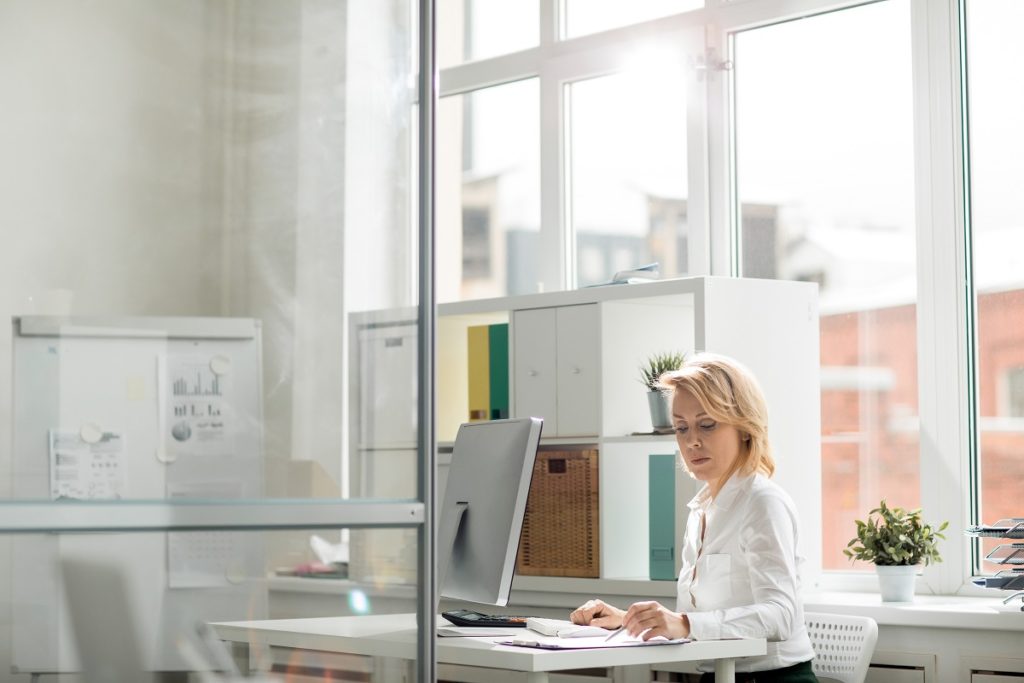 Serious office worker concentrating on reading documents by her workplace