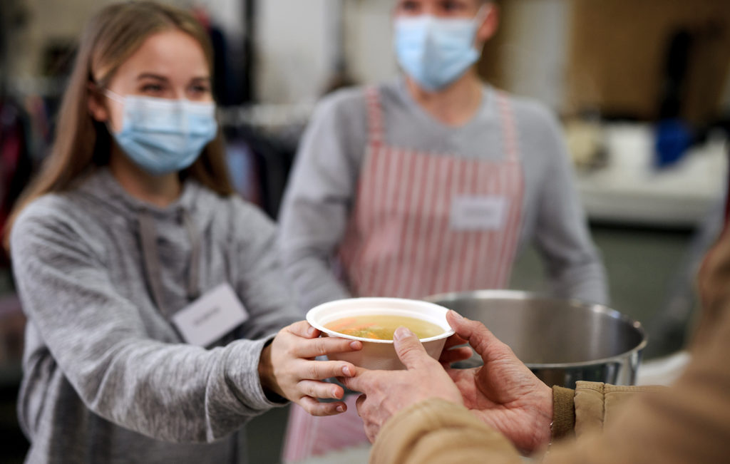 Soup kitchen volunteer handing out a bowl of hot soup